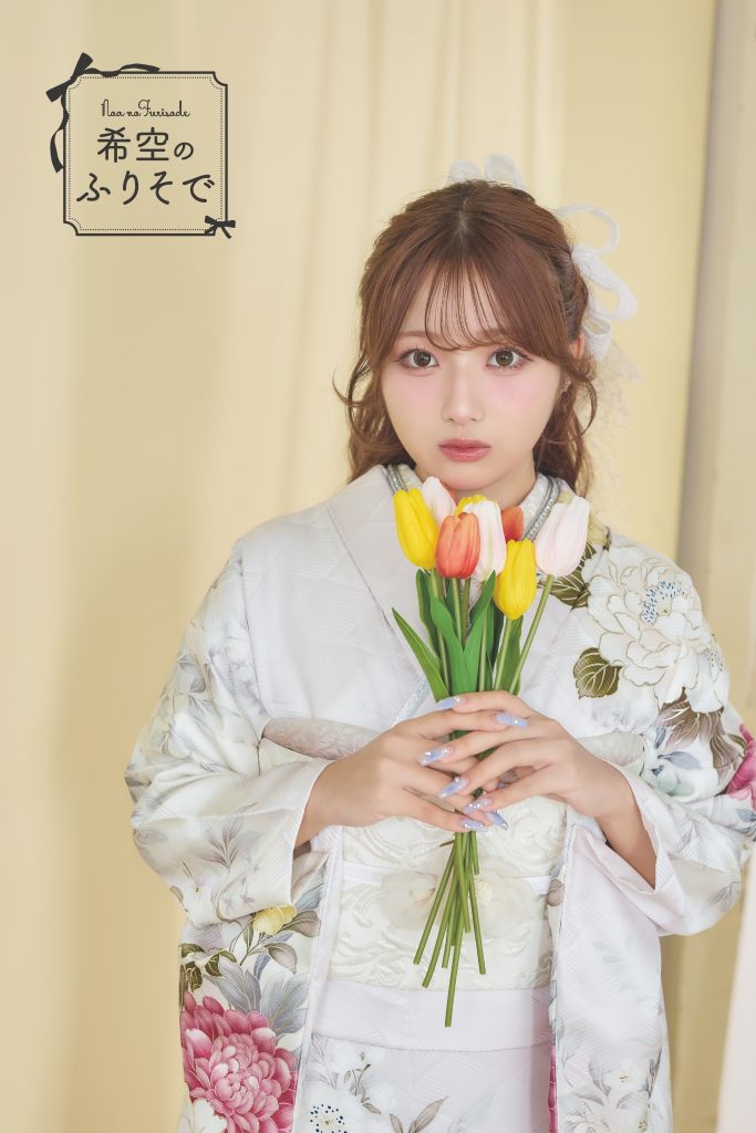 「白地に淡いピンクや黄色の花柄が描かれた振袖を着た希空(のあ)が、清楚で柔らかな雰囲気でポーズをとる写真。」