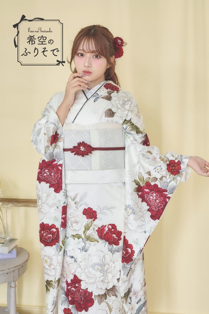 「白地に深紅の花柄振袖を着た希空(のあ)が、赤い差し色と花柄を引き立てる上品コーデで立っている写真。」