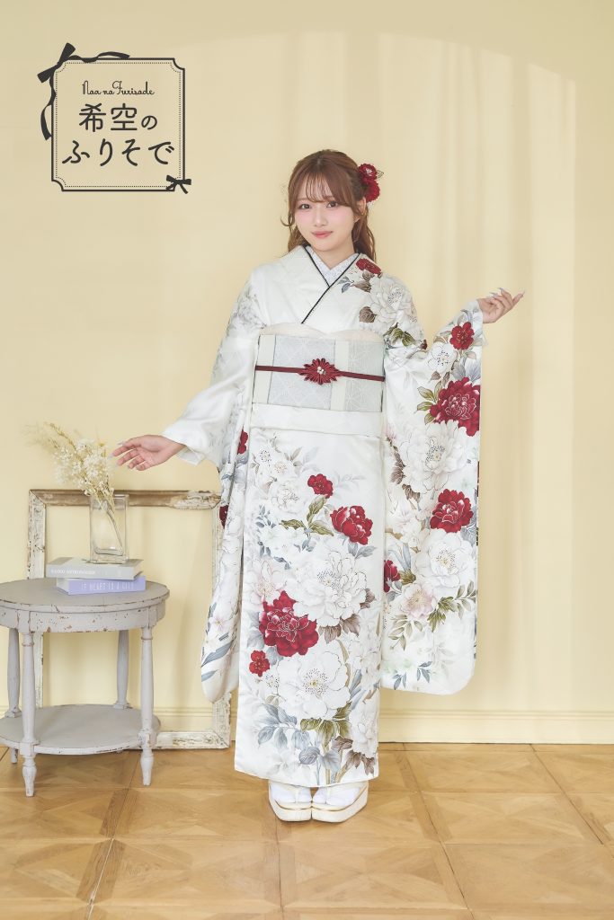 「白地に深紅の花柄振袖を着た希空(のあ)が、赤い差し色と花柄を引き立てる上品コーデで立っている写真。」