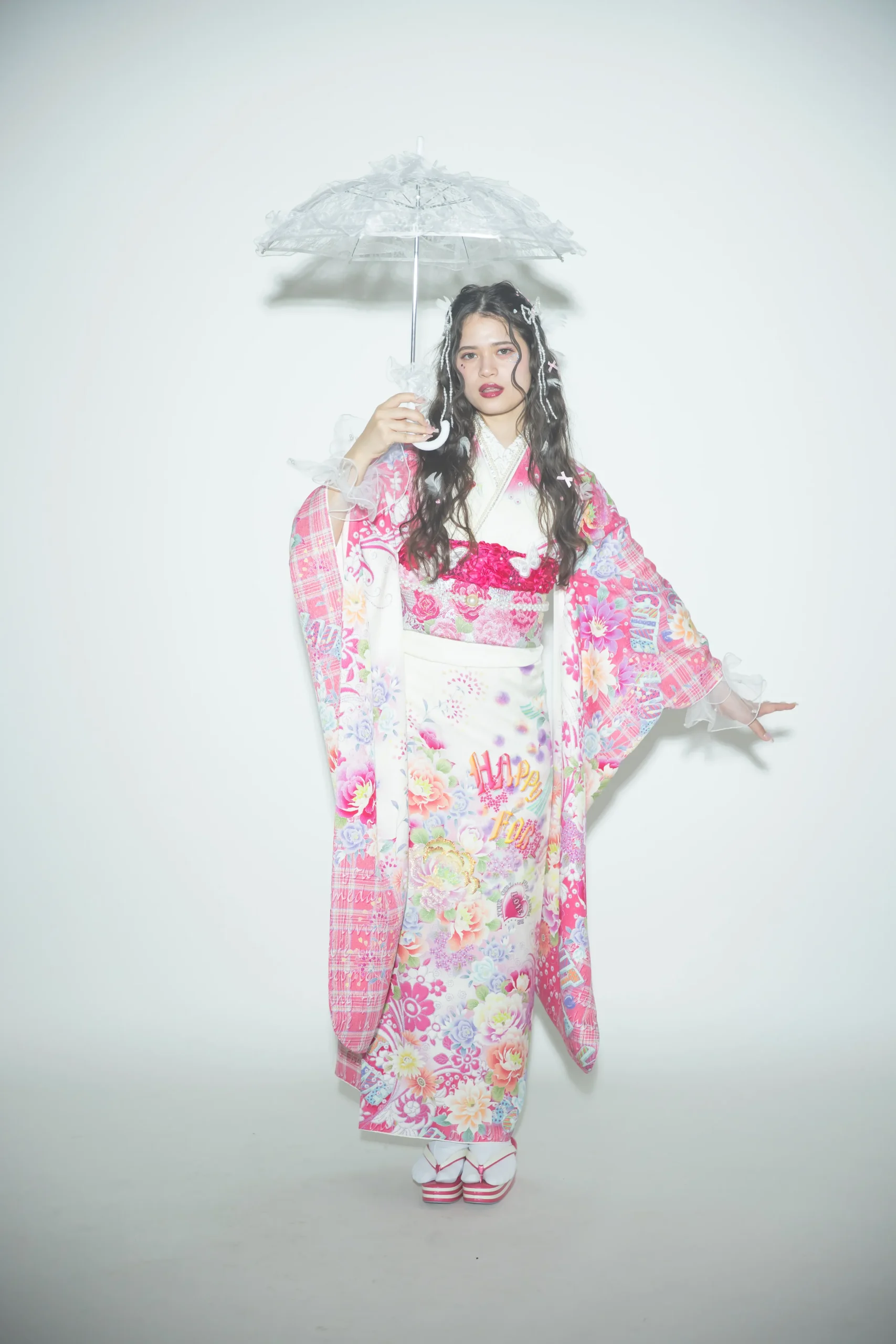 白地にピンクを基調とした花柄とロゴデザインが可愛いガーリー振袖を着用した女性の全身スタジオ写真。成人式振袖レンタルPLUM（プラム）岐阜・一宮対応