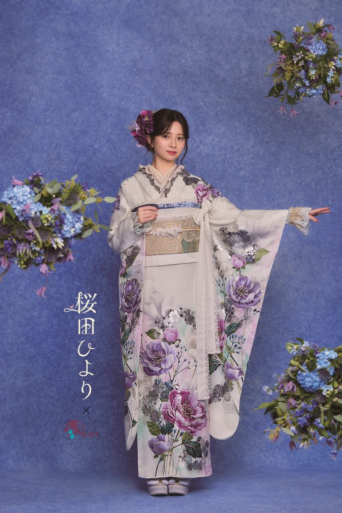 桜田ひより着用の淡色振袖。白地に紫やくすみカラーの花柄が描かれた上品で大人可愛い成人式向け振袖。青系背景と花装飾で落ち着きのある振袖コーディネート。