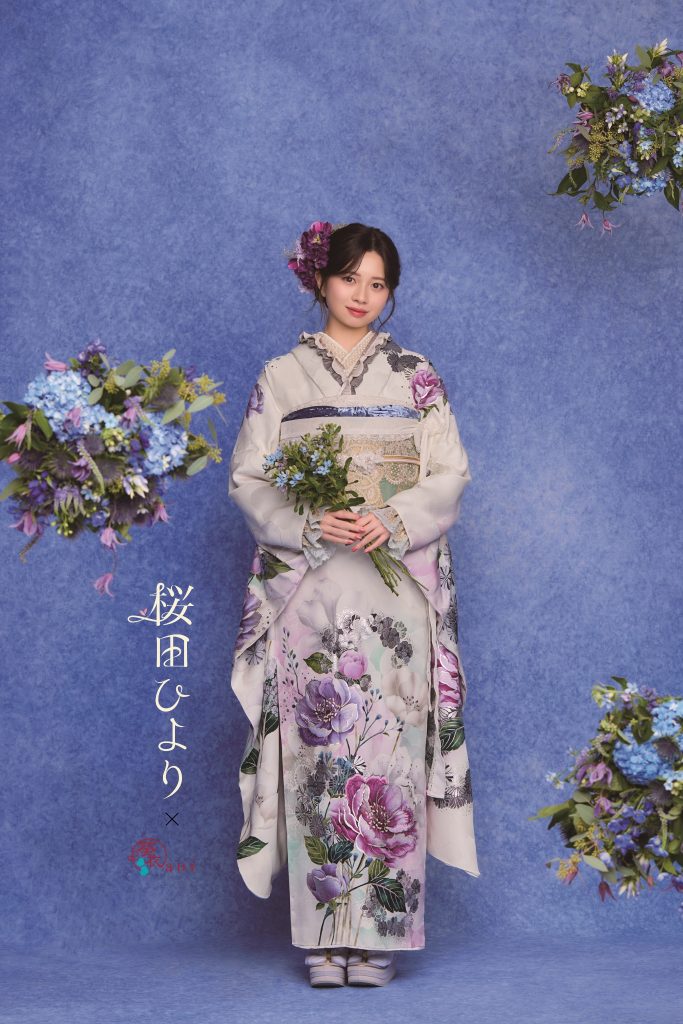 桜田ひより着用の淡色振袖。白地に紫やくすみカラーの花柄が描かれた上品で大人可愛い成人式向け振袖。青系背景と花装飾で落ち着きのある振袖コーディネート。