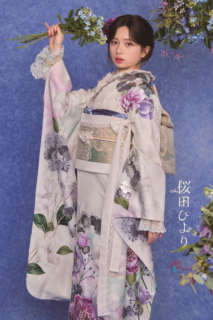 桜田ひより着用の淡色振袖。白地に紫やくすみカラーの花柄が描かれた上品で大人可愛い成人式向け振袖。青系背景と花装飾で落ち着きのある振袖コーディネート。