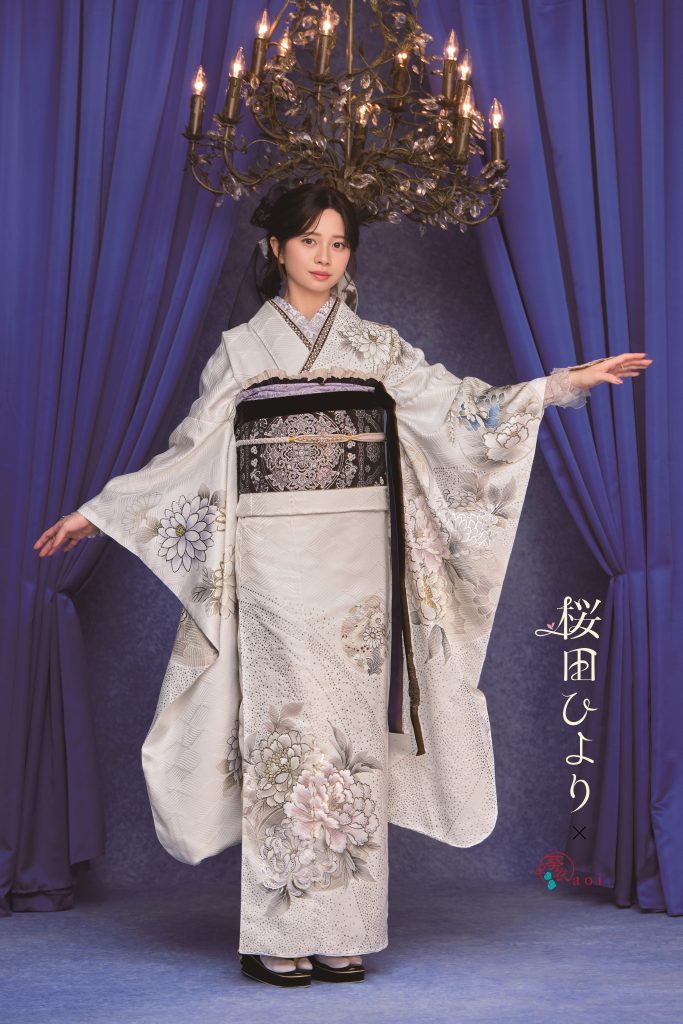 桜田ひより着用の白地振袖。シルバーやグレーの花柄が上品に描かれた大人っぽい成人式向け振袖。シャンデリアとブルー背景でクラシックかつ洗練された振袖コーディネート。