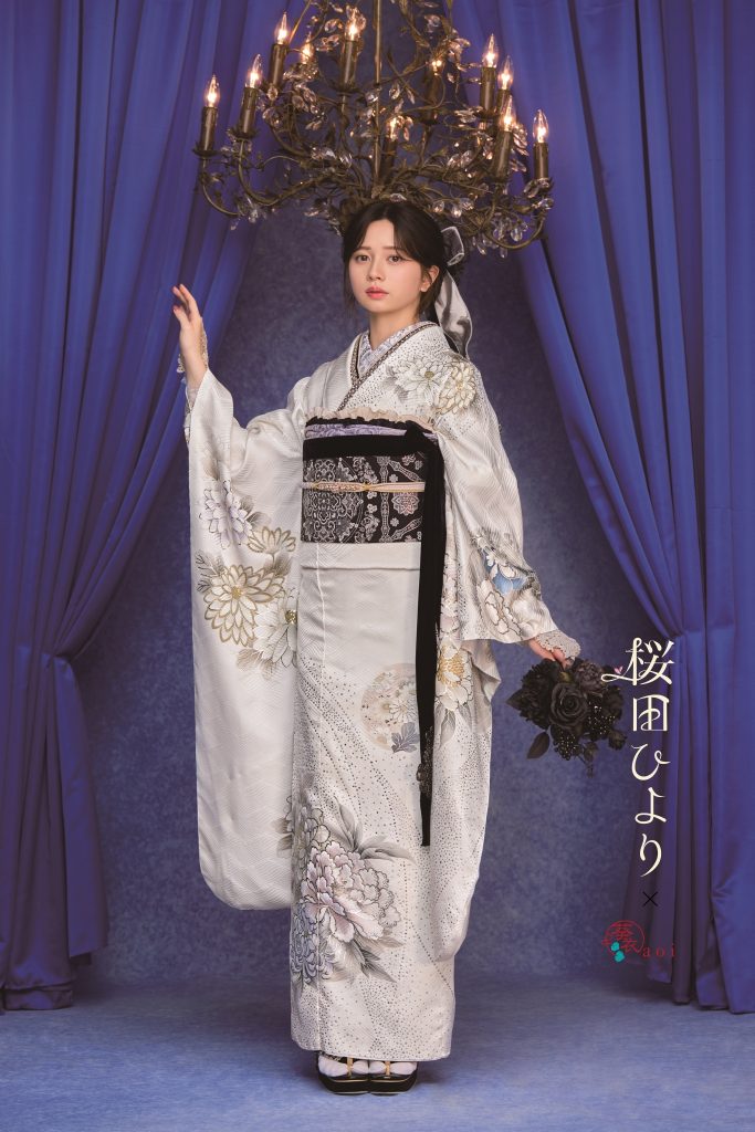 桜田ひより着用の白地振袖。シルバーやグレーの花柄が上品に描かれた大人っぽい成人式向け振袖。シャンデリアとブルー背景でクラシックかつ洗練された振袖コーディネート。