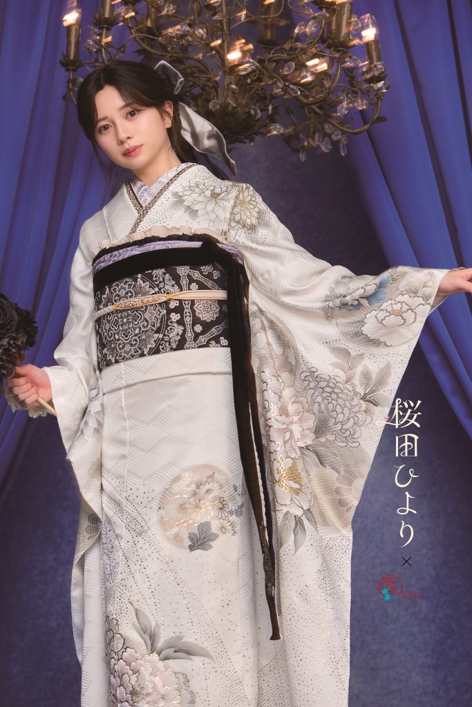 桜田ひより着用の白地振袖。シルバーやグレーの花柄が上品に描かれた大人っぽい成人式向け振袖。シャンデリアとブルー背景でクラシックかつ洗練された振袖コーディネート。