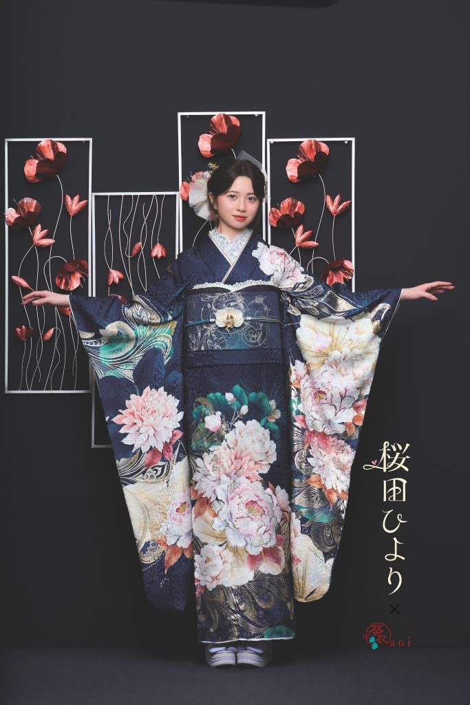 桜田ひより着用の紺地振袖。ネイビーを基調に大輪の牡丹や花柄が描かれた、シックで華やかな成人式向け振袖。黒背景とアートフラワー装飾で写真映えする振袖コーディネート。