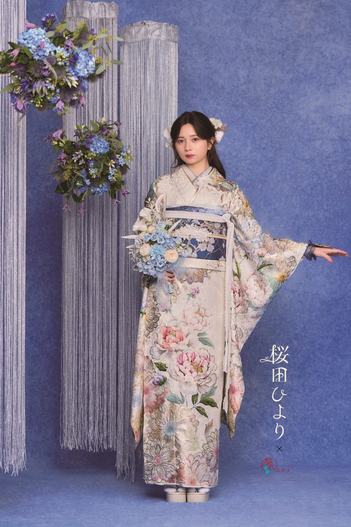 桜田ひより着用の白地×赤茶色振袖。大輪の牡丹と花柄が華やかに描かれた成人式向け振袖スタイル。ピンクの花装飾背景で上品かつ可憐な雰囲気の振袖コーディネート。