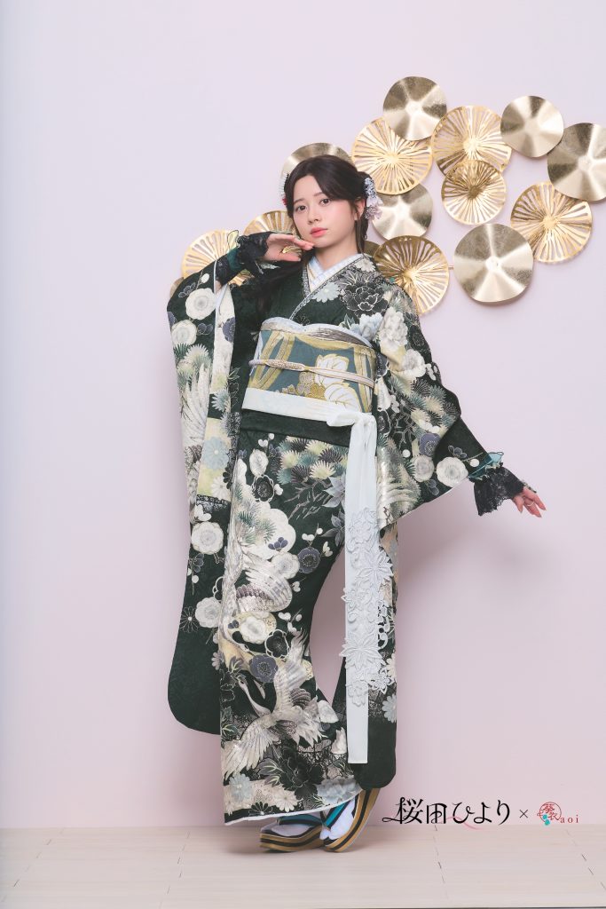 桜田ひより着用の深緑系振袖。松や鶴などの古典柄と花文様が描かれた、格式と華やかさを兼ね備えた成人式向け振袖。ゴールド装飾背景で上品かつモダンな振袖コーディネート。